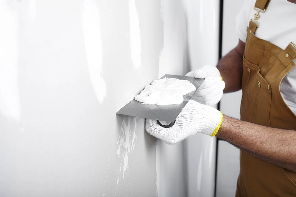 Peintre professionnel en combinaison bleue et casquette blanche applique de la peinture blanche au rouleau sur un mur intérieur