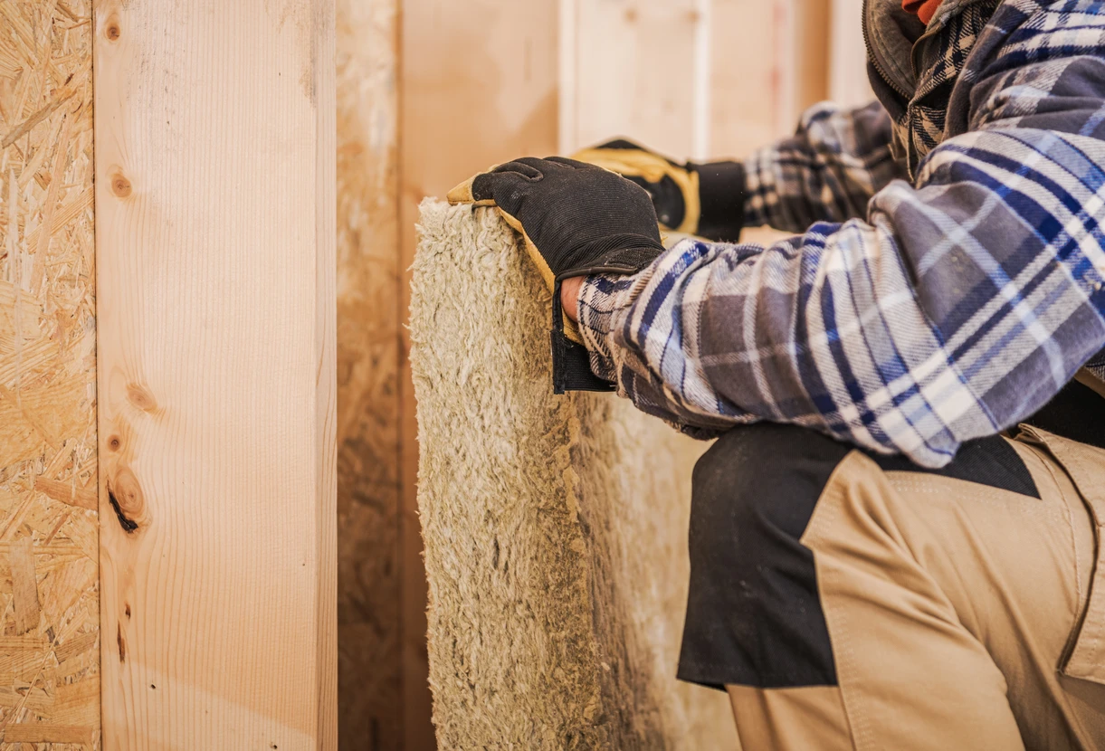 Chantier de construction intérieur avec ouvriers installant l'isolation thermique entre montants bois