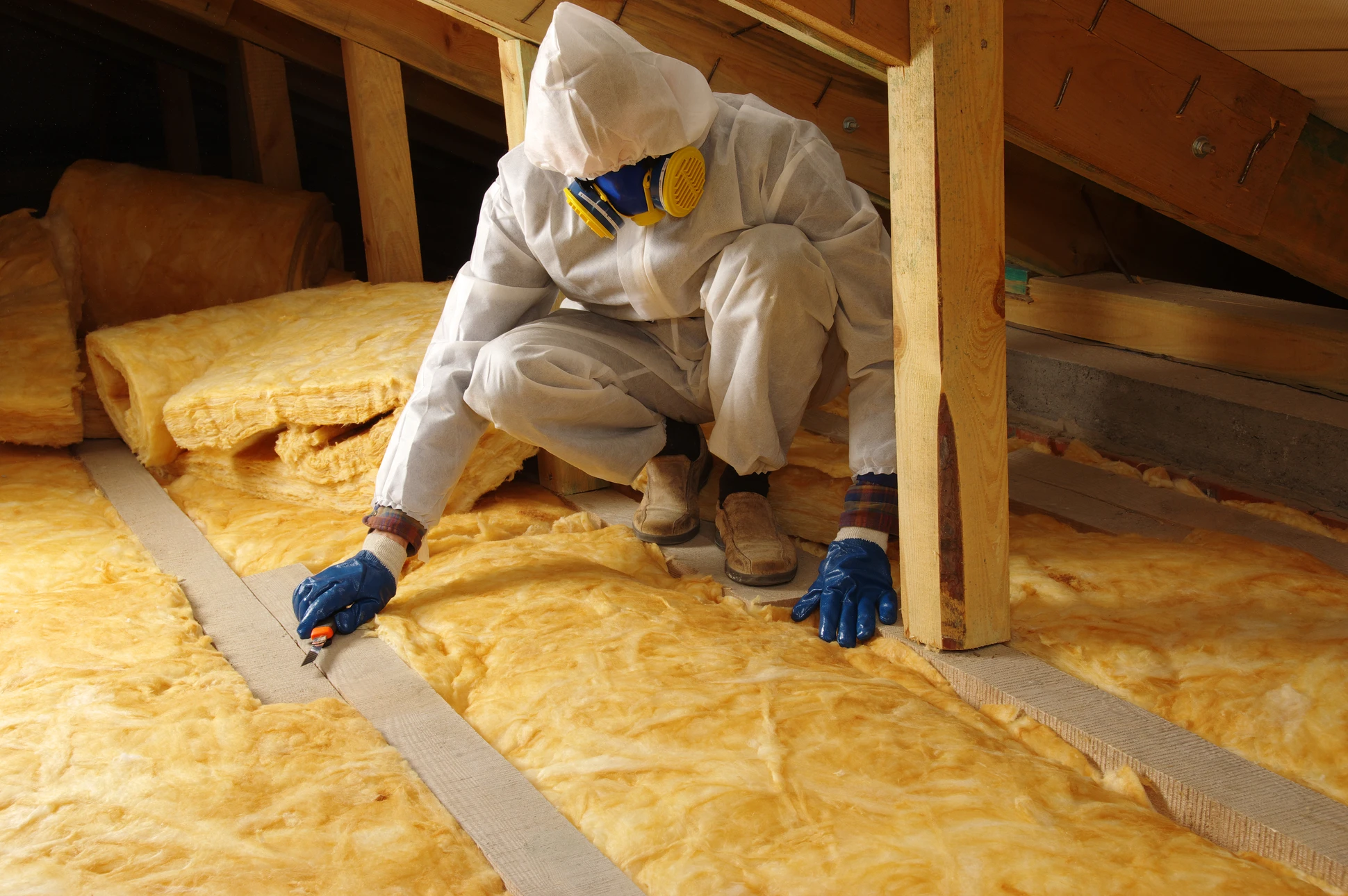 Ouvrier en casque de sécurité installe de l'isolation thermique dans les combles d'une habitation