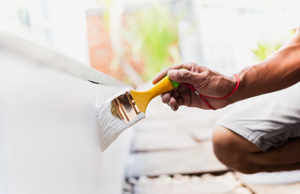 Personne appliquant de la peinture blanche sur un mur intérieur avec un pinceau plat