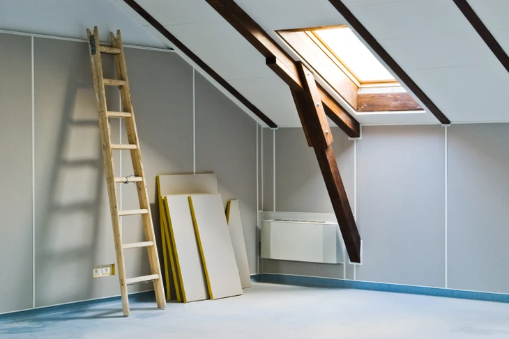 Intérieur d'une maison en construction avec charpente bois apparente et isolation en laine minérale jaune entre les montants