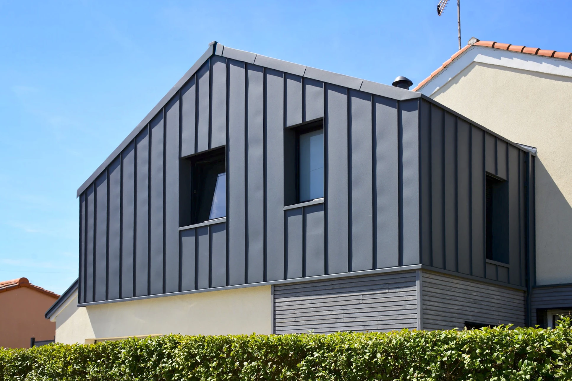 Façade extérieure d'une maison traditionnelle avec bardage bois vertical grisé et soubassement en pierre naturelle