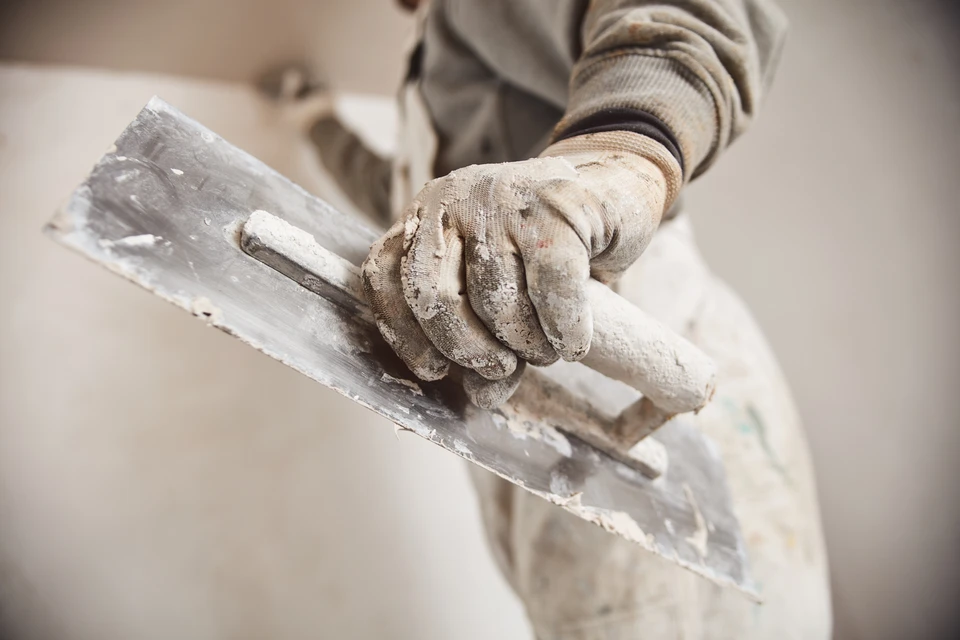 Homme travaillant à genoux sur plancher intérieur, découpant matériau isolant blanc avec cutter